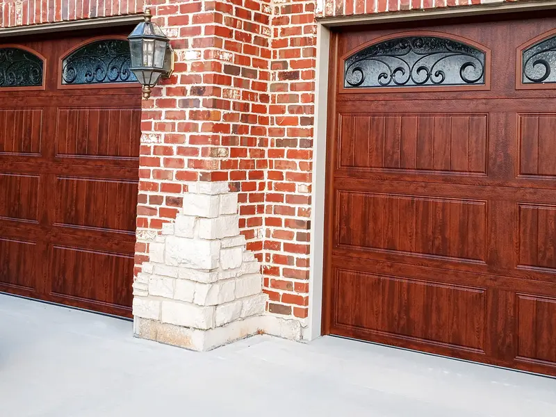 Wood-grain garage door with decorative arched windows on a brick home